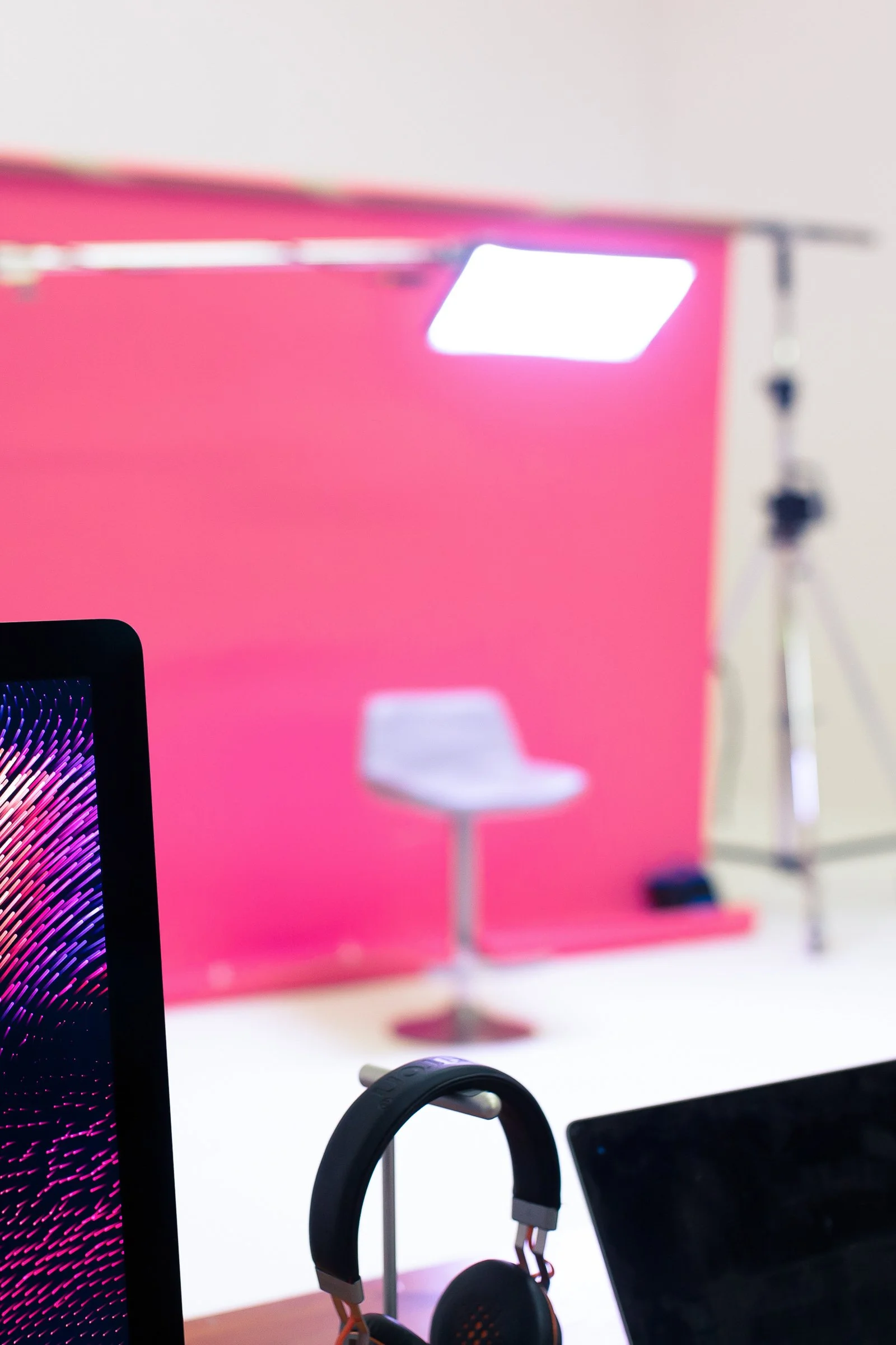 A carefully lit studio setup with a pink backdrop, stool and production equipment